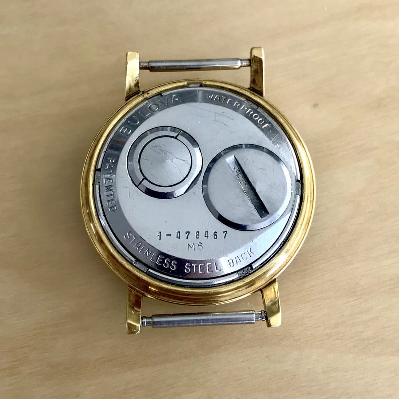 Back display of a vintage wristwatch with text that reads "Bulova," "Waterproof," "Stainless Steel Back," and "Patented." Text includes serial and movement date numbers.